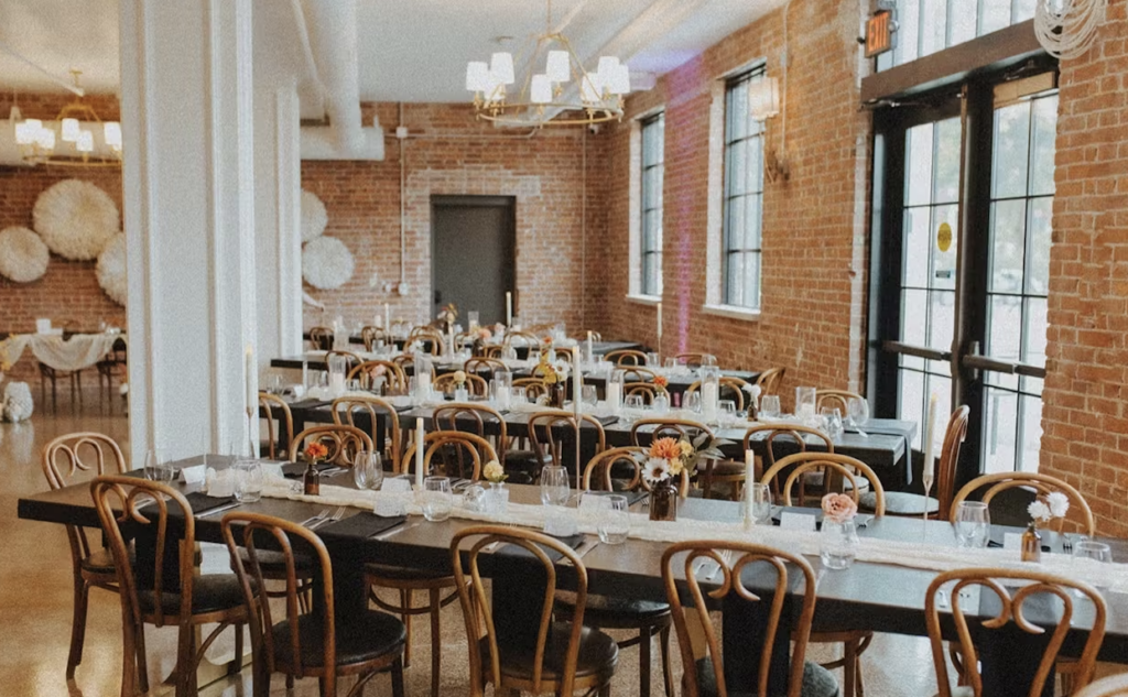 A wedding reception set up in The Hatchery in La Crosse, WIsconsin complete with brick walls, and wooden tables and chairs with runners.